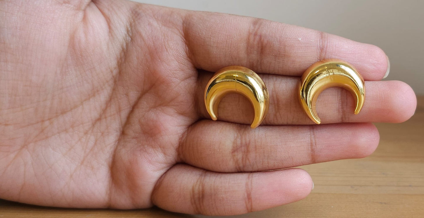 Gold crescent-shaped earrings held in a hand against a neutral background